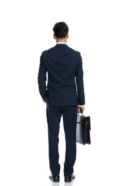 attractive businessman holding briefcase with one hand in pocket, wearing a suit and tie against white background