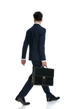 handsome businessman walking, looking away and holding briefcase, wearing a suit and tie against white background