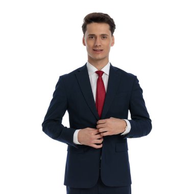 young businessman closing his jacket and smiling, wearing a suit and tie against white background