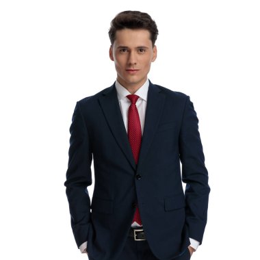 young businessman holding hands in pockets with cute smile, wearing a suit and tie against white background