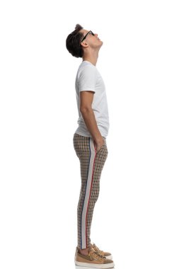 side view of cool fashion man with glasses looking at the sky and wishing while posing with hands in pockets on white background