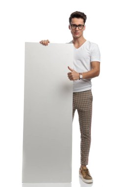casual young man showing white billboard and making thumbs up on white background 