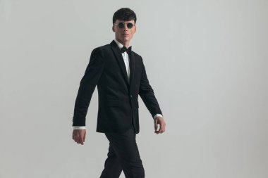 Portrait of handsome businessman walking around and posing, standing, wearing a black tuxedo and sunglasses, in a fashion pose