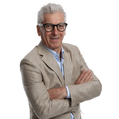 portrait of old man in his 60s wearing beige suit with open collar shirt smiling and crossing arms on white background