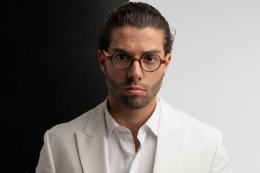 Portrait of young smart casual man looking at the camera with serious face, standing, wearing eyeglasses against black and gray background