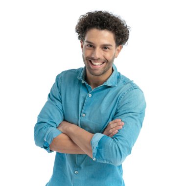portrait of happy casual man with curly hair smiling and crossing arms on white background in studio