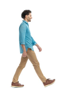 side view of happy casual man with curly hair smiling and walking in front of white background in studio