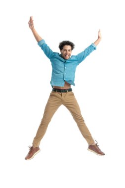 attractive enthusiastic man jumping in the air and holding arms above head, being happy and smiling on white background in studio