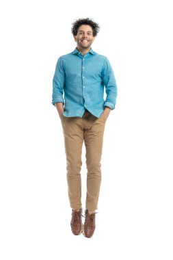 full body picture of handsome turkish man smiling and jumping in the air with hands in pockets in front of white background in studio