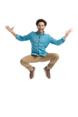 enthusiastic man with curly hair jumping in the air and opening arms, being excited and laughing on white background in studio