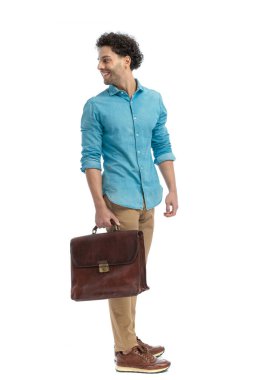 happy turkish man looking over shoulder and smiling while holding suitcase in front of white background