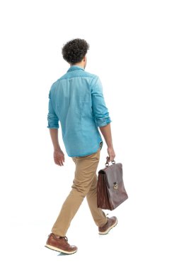 back view of casual curly hair man walking and holding suitcase in front of white background in studio
