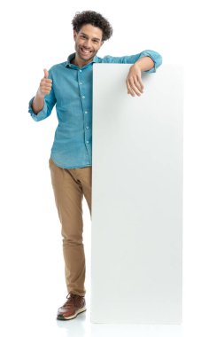happy young man showing blank billboard and making thumbs up gesture, smiling and posing on white background