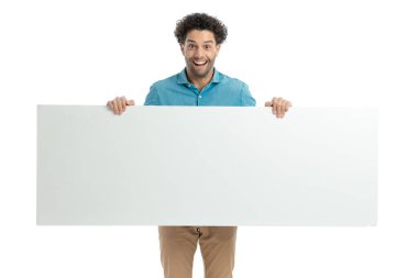 excited casual guy with curly hair laughing while holding empty board in front of white background in studio