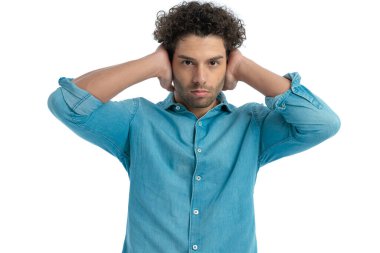 handsome man with curly hair in denim shirt covering his ears and being done with listening in front of white background