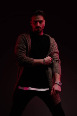 Portrait of attractive man pulling his cardigan with tough attitude, standing, in a fashion pose