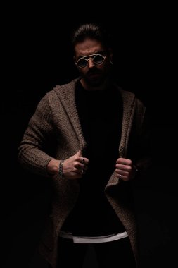 Portrait of handsome man arranging his cardigan and looking at the camera, standing, in a fashion pose