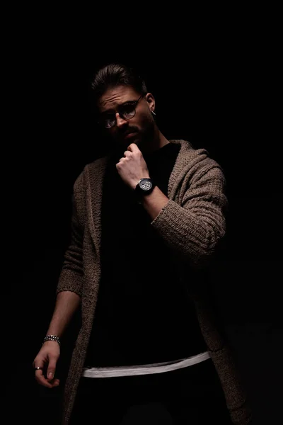 Portrait of young male model slowly scratching his beard, standing, in a fashion pose