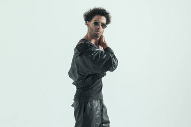 young casual man turning his body and touching his neck, wearing a leather costume in a fashion pose