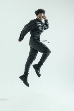 young casual man jumping and dancing with dynamic moves, wearing a leather costume in a fashion pose