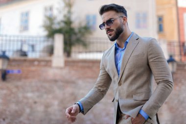 portrait of sexy young businessman in suit with blue shirt and glasses looking away and walking outdoor in a city from Transylvania