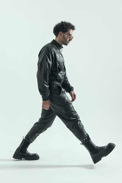 sexy casual man walking with attitude, wearing a leather costume in a fashion pose