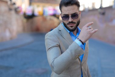 portrait of attractive bearded businessman holding arm in fashion pose and looking down while confidently posing outdoor in an old city