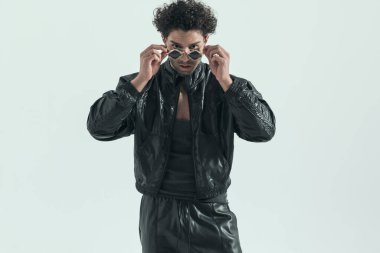 sexy casual man fixing his sunglasses, wearing a leather costume in a fashion pose