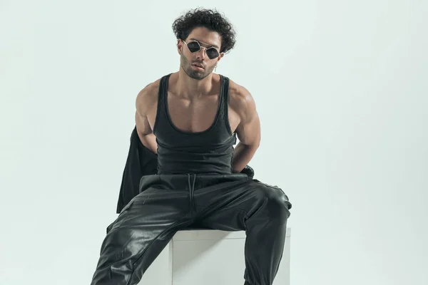 handsome casual man undressing himself and showing his muscles, wearing a leather costume in a fashion pose