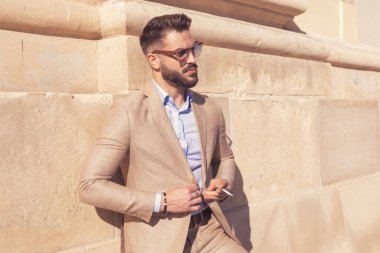 Yakışıklı iş adamının portresi ceketini açıyor ve sigarasını tutuyor, dışarıda güneş gözlüğü takıyor, eski bir ortaçağ kasabasında.