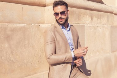 Eski ortaçağ kasabasında avuçlarını ovuşturan, duvara yaslanan, güneş gözlüğü takan seksi iş adamının portresi.