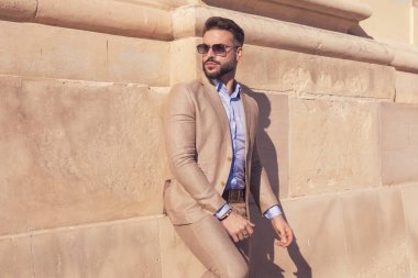 Yakışıklı iş adamının portresi duvara yaslanıyor ve eski ortaçağ kasabasında güneş gözlüğü takıyor.