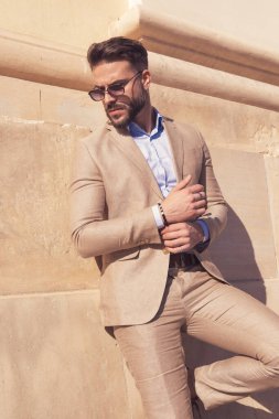 Eski ortaçağ kasabasında, duvarlara yaslanıp kollarını düzelten güneş gözlüğü takan genç iş adamının portresi.