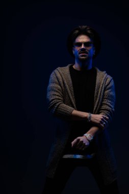 Elini erkeksi bir çerçevede tutan, koyu renk stüdyo arka planda bordo şapka, gözlük ve yün ceket giyen çekici bir adamın portresi.