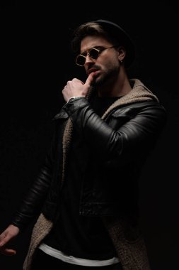 Seksi, genç moda adamı siyah arka planda dudaklara dokunurken gözlerini kaçırıyor.