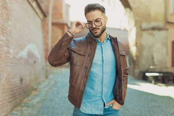 若いカジュアルな男の肖像画眼鏡を配置し ポケットに手を入れて 革のジャケットを着て 古い中世の町で屋外 — ストック写真