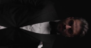 Seksi iş adamı smokinini ayarlıyor, dudaklarına dokunuyor ve arkasını dönüyor.