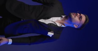 Manken ceketini düzenliyor, ellerini cebine koyuyor, seksi videoda çenesine dokunuyor.