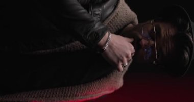 Seksi sıradan bir adam dudaklarını bastırıyor, ceketini ve şapkasını ayarlıyor ve ışıklarla birlikte kayboluyor.