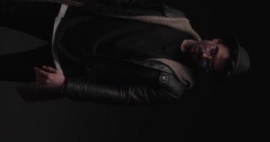 Siyah deri ceketli seksi, sert, sıradan bir adam bir moda videosunda kollarını göğsünde kavuşturuyor.