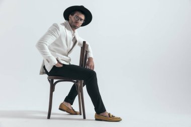 Koltuğun üzerinde oturan, gri arka planda el ele oturan kendine güvenen zarif bir adamın yan görüntüsü.