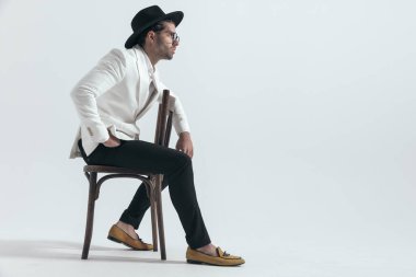 Yakışıklı adamın yan görünüşü ahşap koltukta oturuyor, el ele ve gri arka plana bakıyor.