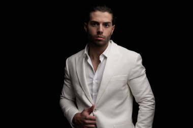 Beyaz ceketi düzenleyen ve siyah arka planda poz veren zarif seksi bir adamın portresi.