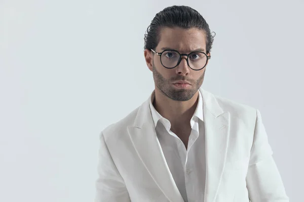 cool fashion man with glasses wearing white jacket suit and open collar shirt in front of grey background