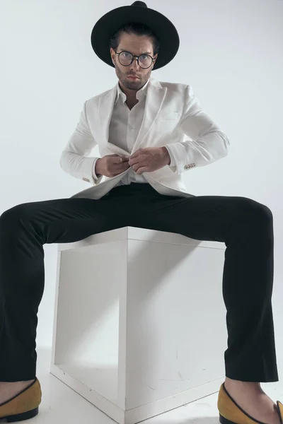 Şapkalı Gözlüklü Beyaz Ceketli Beyaz Arka Planda Oturan Moda Adamı — Stok fotoğraf