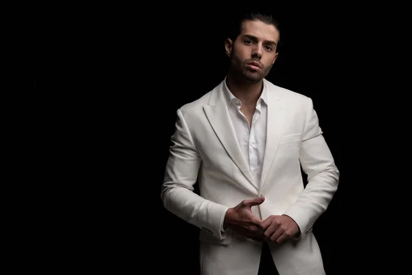 attractive elegant man wearing open collar shirt with white suit touching fingers and posing on black background