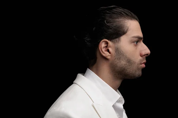 side view of sexy elegant man in white suit with open collar shirt looking to side and posing