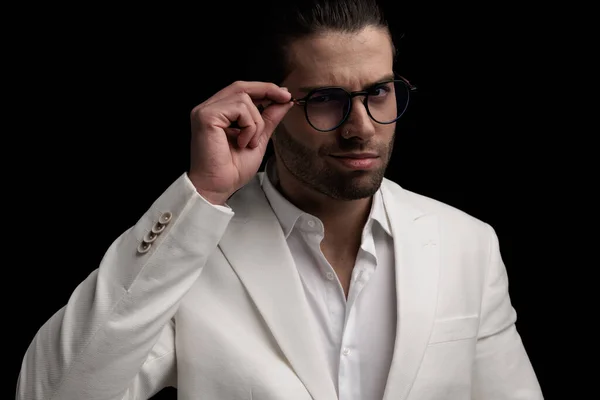sexy elegant man in white suit smiling and adjusting glasses in front of black background