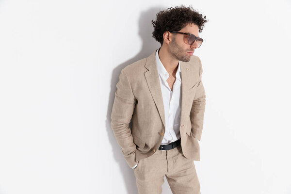 sexy stylish man with curly hair laying on the wall with hands in pockets and looking away on grey background