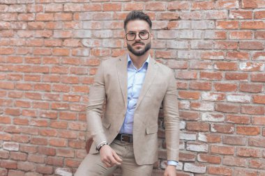 Eski bir ortaçağ kasabasında, duvara yaslanmış, tutumuyla poz veren ve gözlük takan seksi iş adamının portresi.